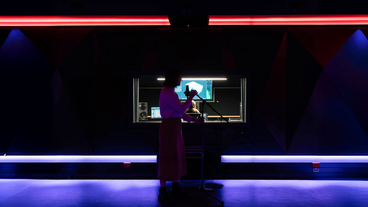 A dark lit image of a singer in a sound booth
