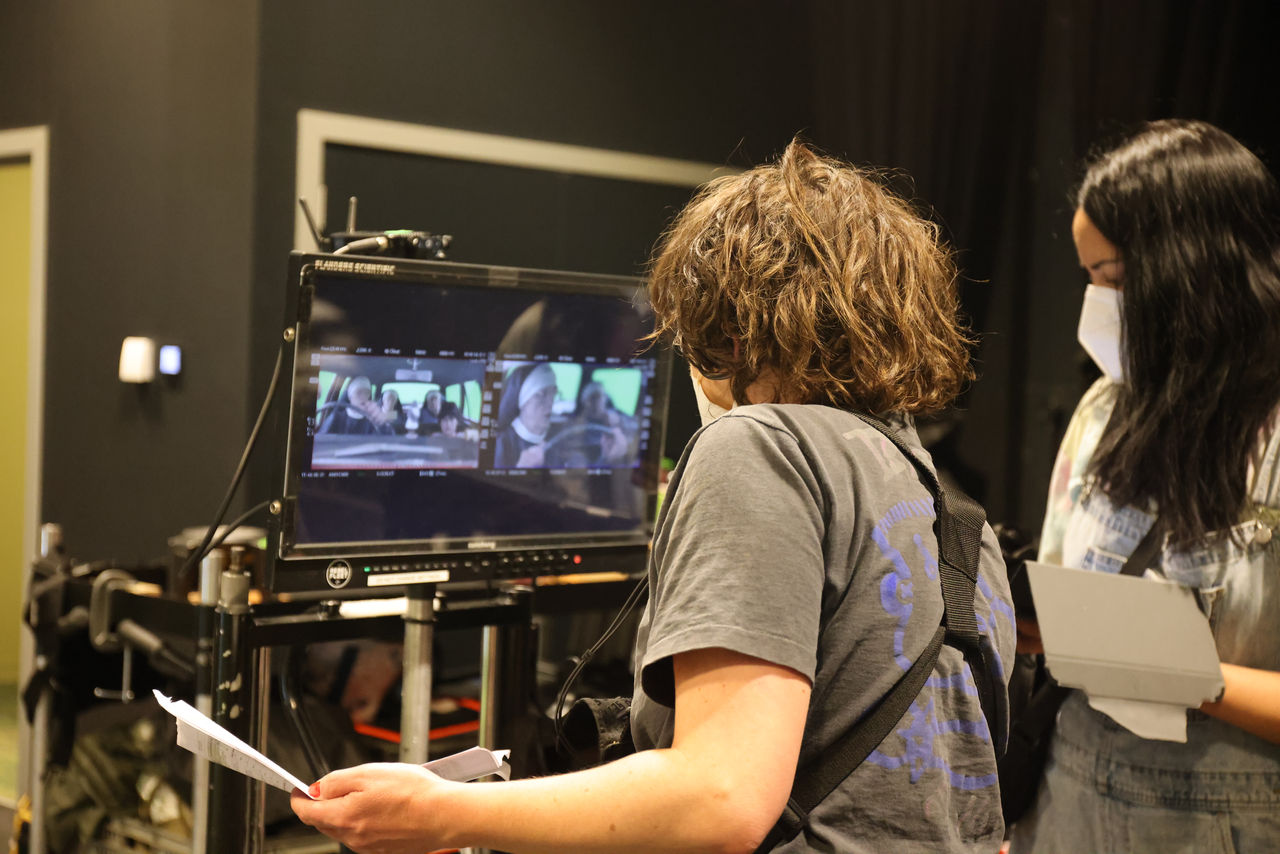 Image of 2x technicians looking at a camera of the live action from behind the scenes of the Holy Days filming.